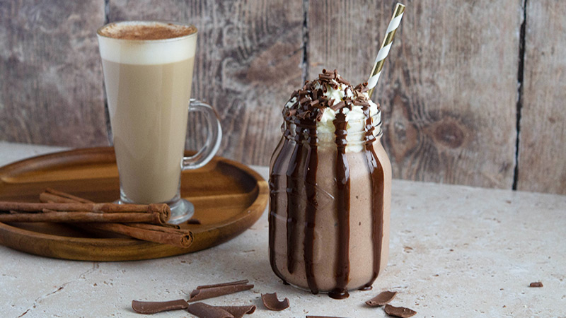 a flavoured latte on awooden tray with a chocolate frappe in a mason jar with chocolate sauce
